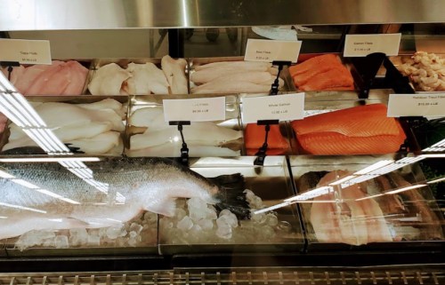 A display case filled with various types of fresh fish and seafood on ice, labeled with prices.