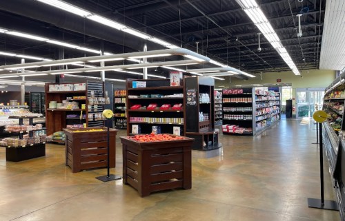 A spacious grocery store aisle with shelves stocked with various products and bright overhead lighting.