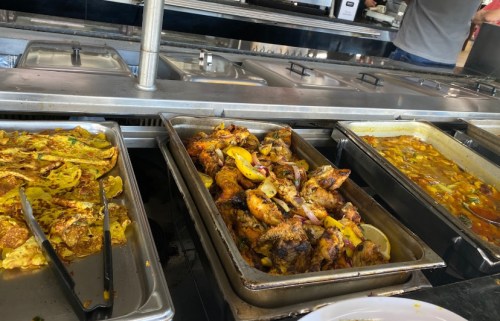 A buffet display featuring various dishes, including grilled chicken, curries, and flatbreads in metal trays.