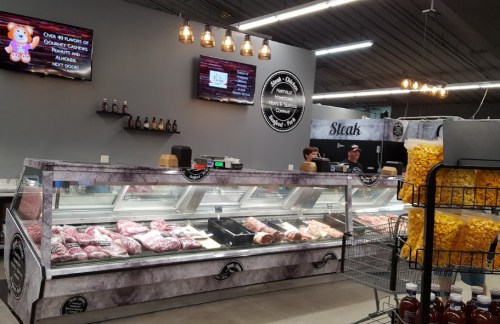 A meat counter displaying various cuts of meat, with staff and signage in a well-lit store.