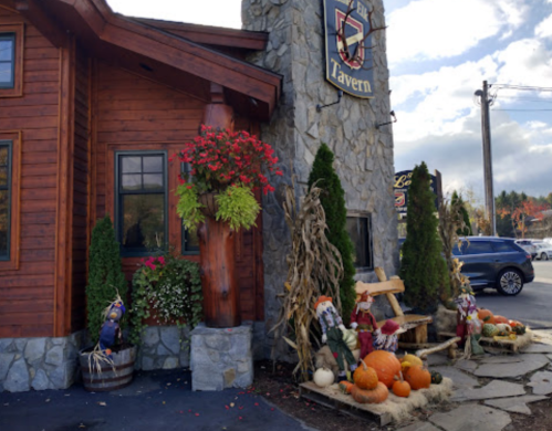 A rustic tavern exterior with stone walls, flower pots, pumpkins, and autumn decorations.
