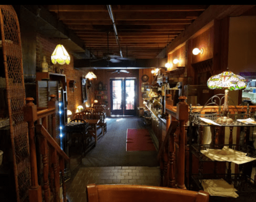 Cozy restaurant interior with wooden beams, warm lighting, and a welcoming atmosphere. Tables and a counter are visible.
