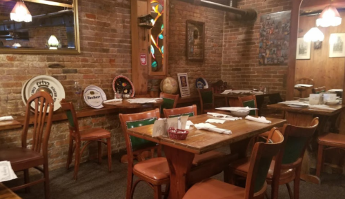 Cozy restaurant interior with wooden tables, chairs, and brick walls, featuring decorative plates and warm lighting.