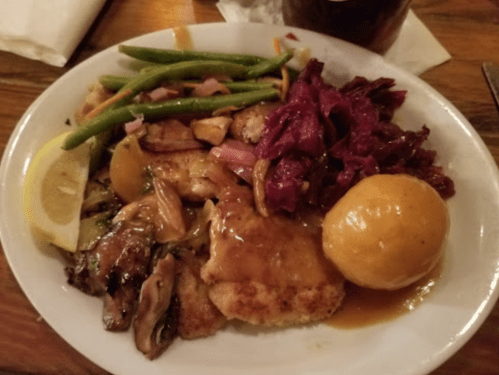 A plate of food featuring fried chicken, green beans, red cabbage, and a biscuit, garnished with a lemon slice.