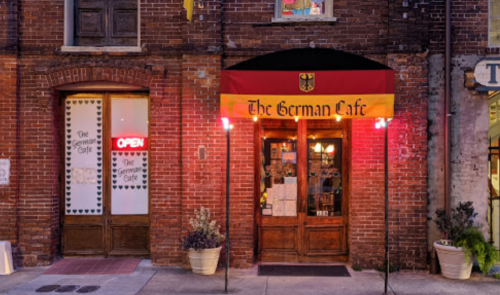 A brick building featuring "The German Cafe" with a red and yellow awning and an open sign in the window.