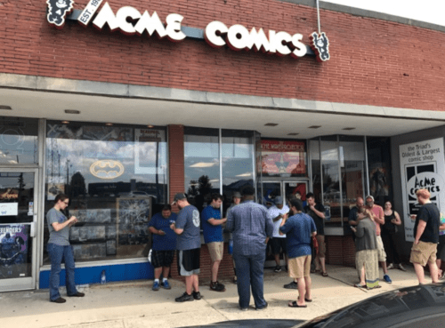 A group of people stands outside Acme Comics, waiting in line in front of the store on a sunny day.