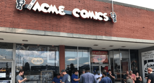 A group of people gathered outside Acme Comics, a brick storefront with a large sign, on a sunny day.