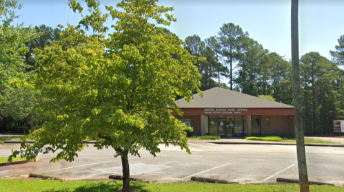 A United States Post Office building surrounded by trees and an empty parking lot.