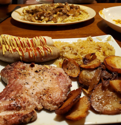 A plate of grilled pork chops, roasted potatoes, sauerkraut, and sausages drizzled with ketchup and mustard.