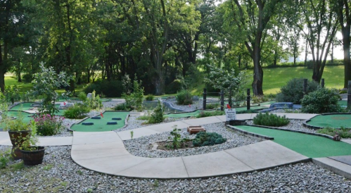 A scenic mini-golf course surrounded by trees and gardens, featuring winding paths and vibrant greenery.