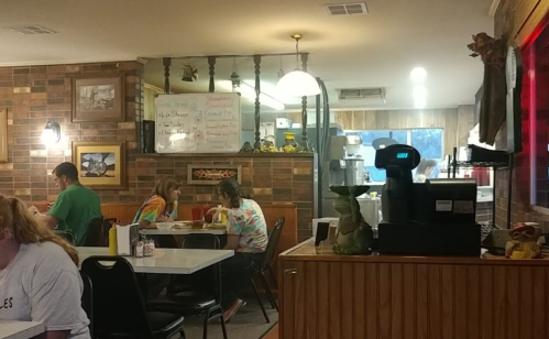 A cozy diner scene with patrons at tables, a coffee machine, and a kitchen area in the background. Warm, inviting atmosphere.