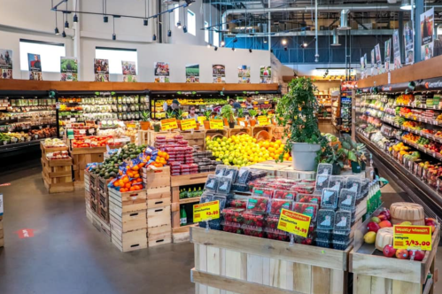 A vibrant grocery store aisle filled with fresh fruits and vegetables in wooden crates and colorful signage.