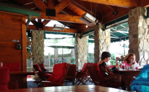 Cozy restaurant interior with wooden beams, stone walls, and red chairs; two people seated at a table.