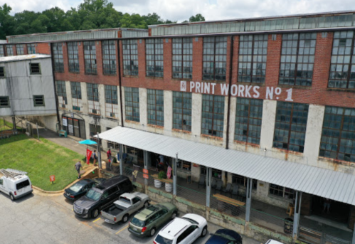 A large, industrial building with "PRINT WORKS NO. 1" on the facade, featuring a covered porch and parked cars.