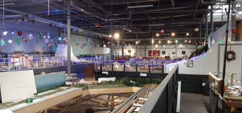 A spacious indoor exhibit featuring model trains, festive decorations, and illuminated displays.