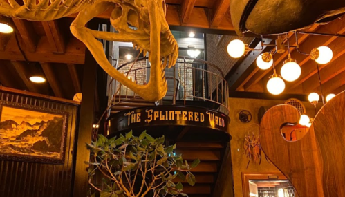 Interior of a themed restaurant featuring a dinosaur skeleton, spiral staircase, and warm lighting.