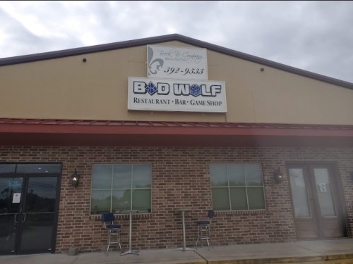 Exterior of a building featuring a sign for "Bad Wolf Restaurant, Bar, Game Shop" with a brick facade and chairs outside.