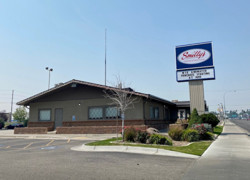 A building with a sign for "Smitty's" on a street, featuring a landscaped area and clear blue sky.