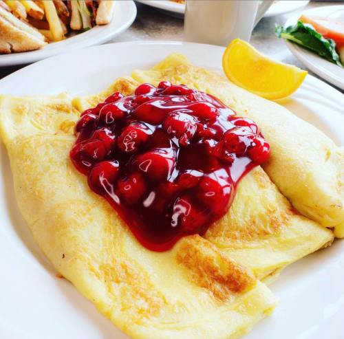 A fluffy omelette topped with cherry sauce and served with a slice of lemon.