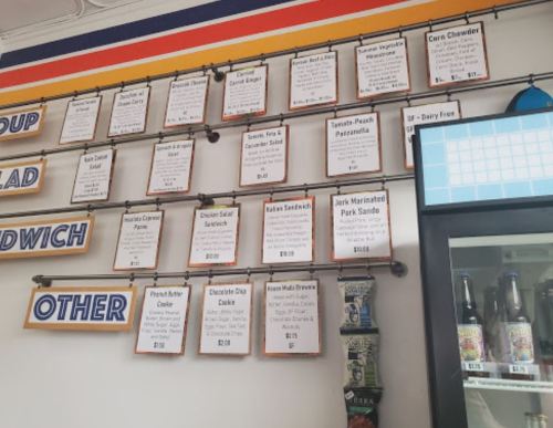 Menu board displaying various food items and prices, including sandwiches, soups, and desserts.
