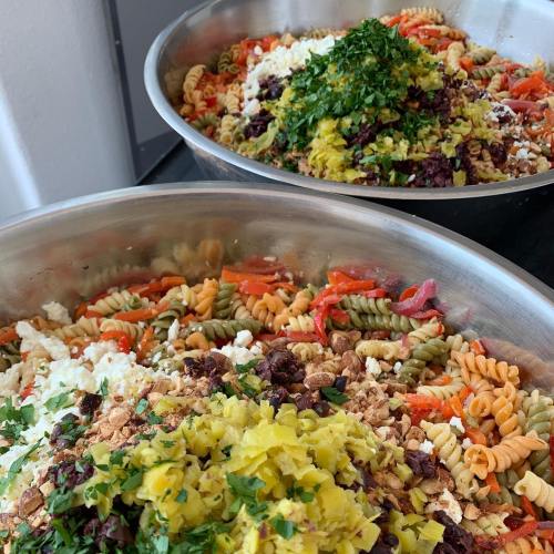 Two large bowls of colorful pasta salad with vegetables, herbs, and toppings, including cheese and olives.