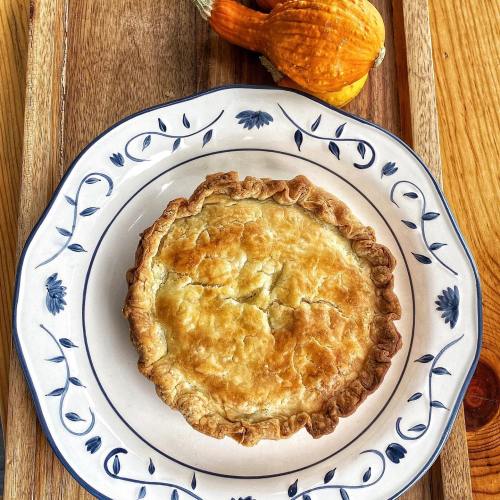 A golden-brown pie on a decorative plate, accompanied by small decorative gourds on a wooden tray.