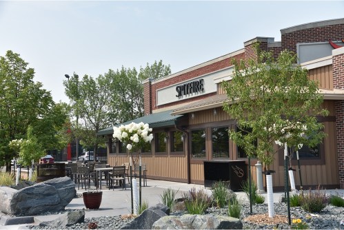 Exterior view of a restaurant with outdoor seating, surrounded by greenery and decorative rocks.