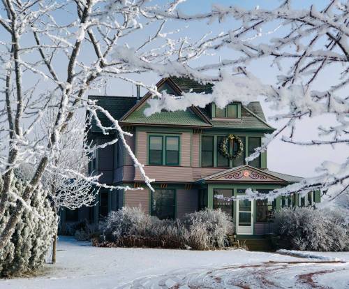 A charming pink house adorned with a wreath, surrounded by snow-covered trees in a winter landscape.