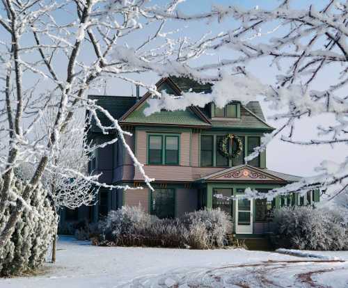 A charming pink house adorned with a wreath, surrounded by snow-covered trees in a winter landscape.