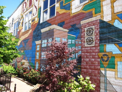 Colorful mural on a building wall featuring abstract designs and greenery in the foreground.