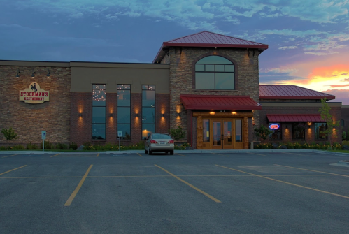Exterior of Stockman's Restaurant at sunset, featuring a stone facade and red roof, with a parking lot in front.