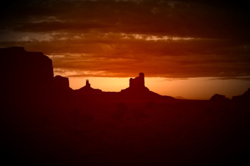 Silhouetted rock formations against a vibrant sunset sky with clouds.
