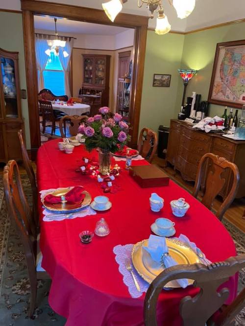 A beautifully set dining table with a red tablecloth, floral centerpiece, and elegant dishware in a cozy dining room.
