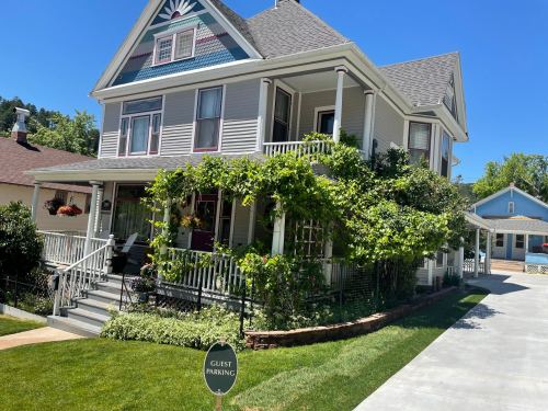 A charming two-story house with a porch, surrounded by greenery and a sign for guest parking in a sunny setting.