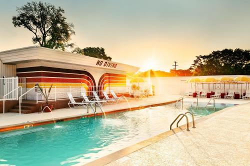 A vibrant pool area at sunset, featuring lounge chairs, umbrellas, and a "No Diving" sign on a colorful building.