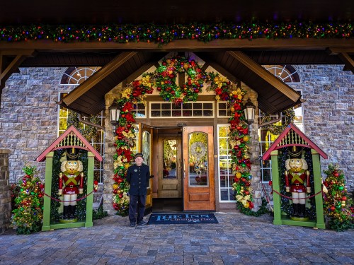 A festive entrance adorned with a wreath, lights, and nutcracker statues, with a person standing in front.