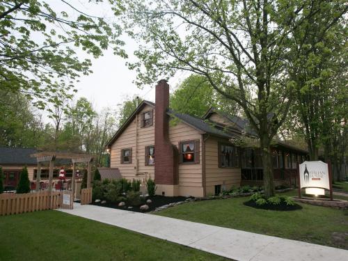 A cozy, two-story house surrounded by trees, featuring a brick chimney and a welcoming sign in the front yard.
