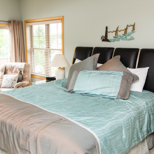 A cozy bedroom featuring a large bed with decorative pillows, a chair, and windows letting in natural light.