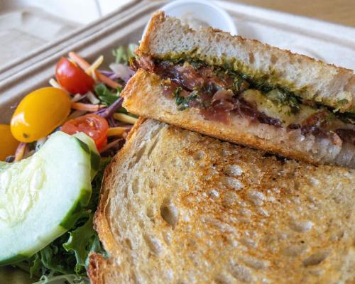 A toasted sandwich with green filling, served with a side salad of cherry tomatoes, cucumber, and mixed greens.