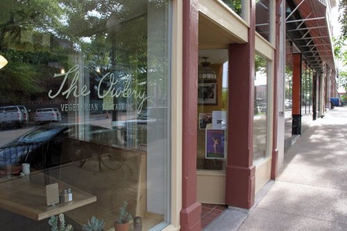 Exterior view of a vegetarian restaurant with large windows and a sidewalk, showcasing a welcoming atmosphere.