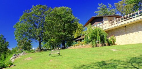 A sunny landscape featuring a modern house, lush green lawn, and trees under a clear blue sky.