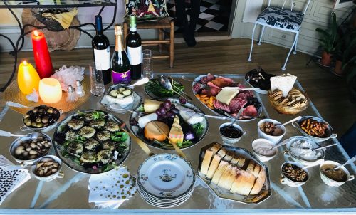 A beautifully arranged table with various dishes, cheeses, fruits, wines, and candles, creating a festive atmosphere.