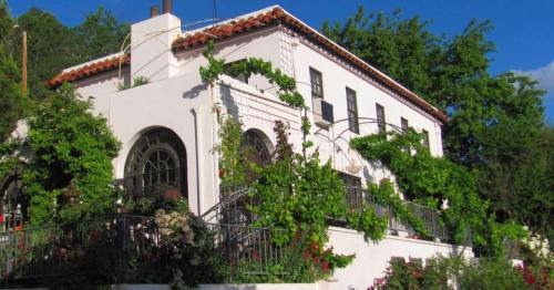A charming white house with a red tile roof, surrounded by lush green vines and blooming flowers.