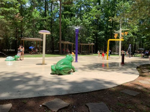 A splash pad in a wooded area with colorful water features and children playing in the water.