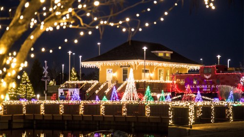 A festive scene featuring a building adorned with colorful holiday lights, surrounded by decorated trees and a train.