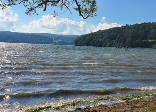 A serene lake scene with gentle waves, surrounded by green hills and a blue sky with scattered clouds.