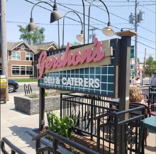 Sign for Gershon's Deli & Caterers, featuring a retro design, with outdoor seating and a clear blue sky in the background.