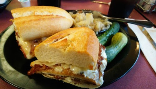 A plate with two sandwiches, pickles, and a side of mashed potatoes.