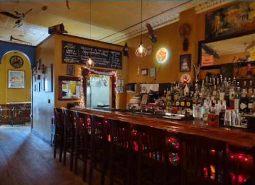 A cozy bar with wooden seating, colorful lights, and a variety of bottles displayed on the shelves. Warm, inviting atmosphere.