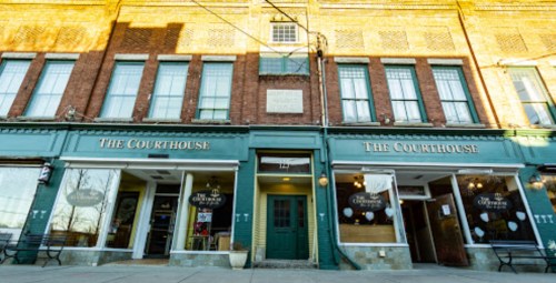 Historic brick building with two storefronts labeled "The Courthouse," featuring large windows and a welcoming entrance.